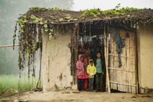 Eine Familie in Nepal steht in der Tür ihrer ärmlichen Hütte aus Bambus und Lehm