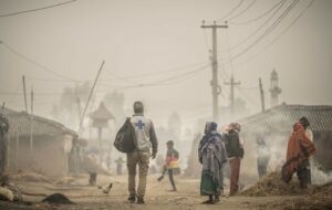 Dorfstraße in Nepal: Im Vordergrund ein paar Menschen, Hütten und Strommasten verschwinden im Nebel